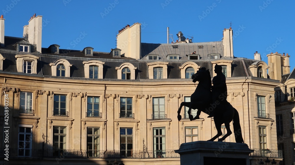 Fototapeta premium Place des Victoires dans la ville de Paris, paysage urbain avec des immeubles haussmanniens et la silhouette de la statue équestre du roi soleil Louis XIV (France)