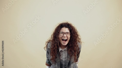 The desperate young woman cried out with a big mouth, leaning forward, fists down. Cretaceous in gray jacket and white shirt, with glasses posing isolated on a beige background in the studio. The