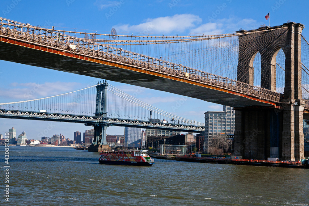 Brooklyn bridge in front of  Manhattan bridge with a tourist boat passing. Sunny winter day with blue sky
