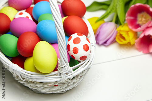 Easter eggs in basket and spring colorful flowers on white wooden table