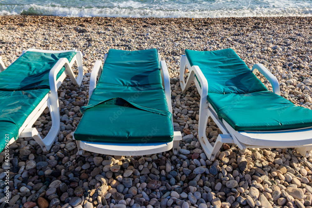 Chaise lounges on a pebble beach. Concept of rest, relaxation, holidays, resort Chaise lounges on a pebble beach. Concept of rest, relaxation, holidays, resort