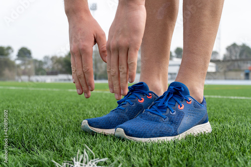 Unrecognized male athlete wearing sports shoes stretching in the stadium after work out.
