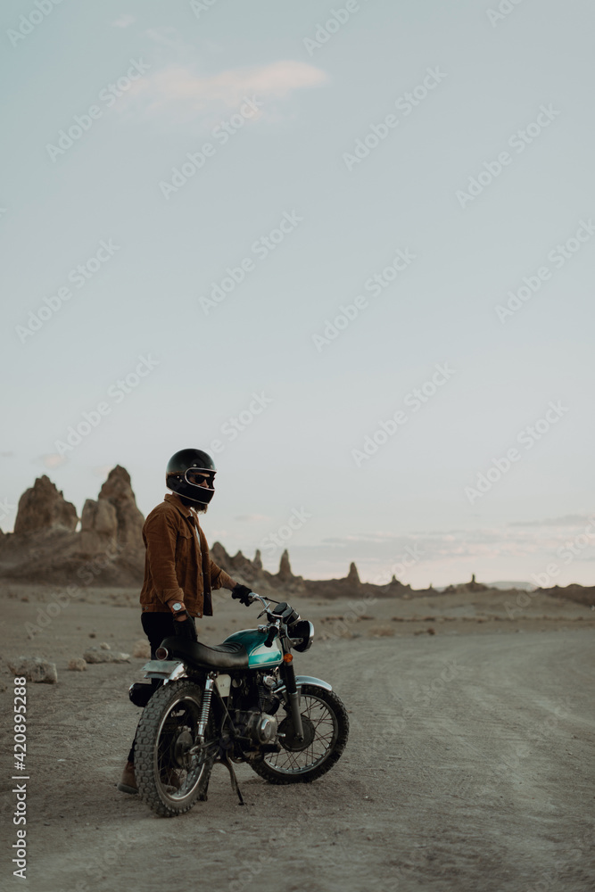 Motorcyclist beside stationary bike in desert, Trona Pinnacles, California, US Motorcyclist beside stationary bike in desert, Trona Pinnacles, California, US