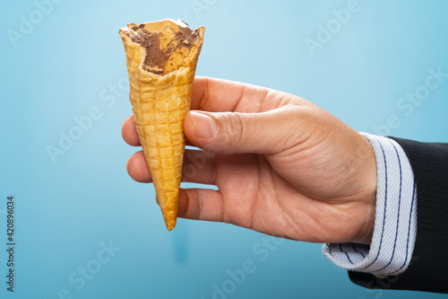 man in suit holding a half eaten coffee flavor ice cream cone with chocolate on blue background
