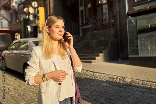 Young beautiful woman walking along city street talking on mobile phone