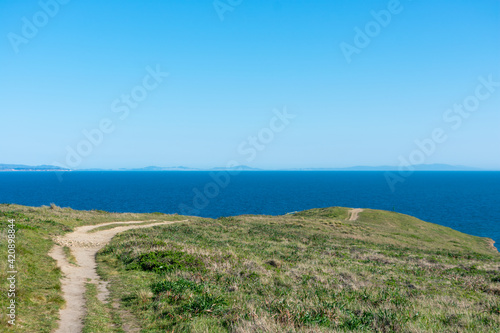 Unpaved hiking trail on Point Reyes Headlands towards Chimney Rock with winter green grass covering cliffs and bluffs at Point Reyes National Seashore, California.