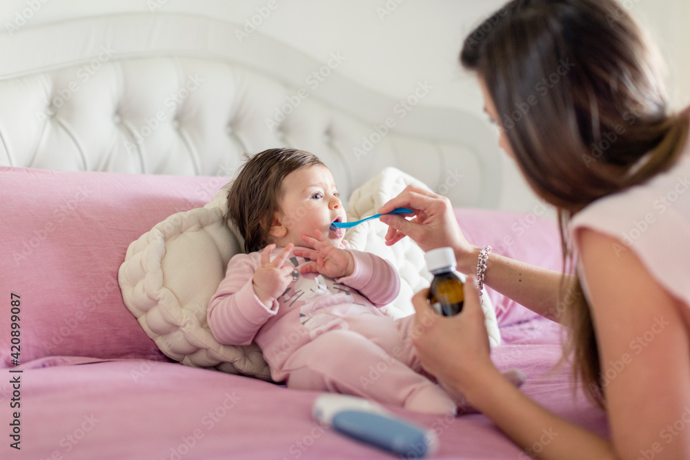 Mother feeding baby girl medicine in bed