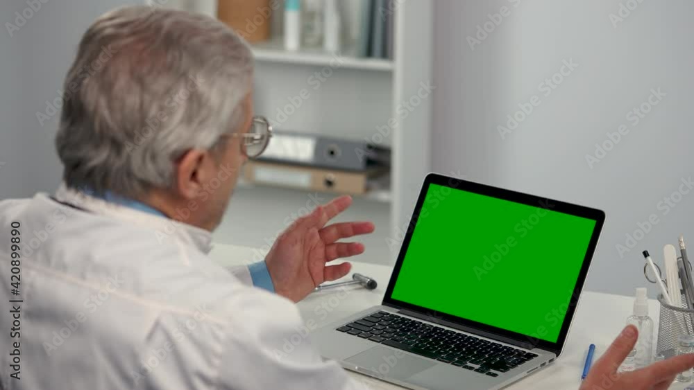 Male doctor consults patient using laptop with green screen chroma key and demonstrates vial with vaccine. Remote online consultation about need for vaccination. Telemedicine. Close up. Slow motion.