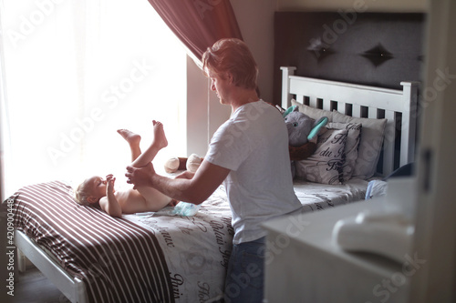 Father changing baby's diaper on bed
