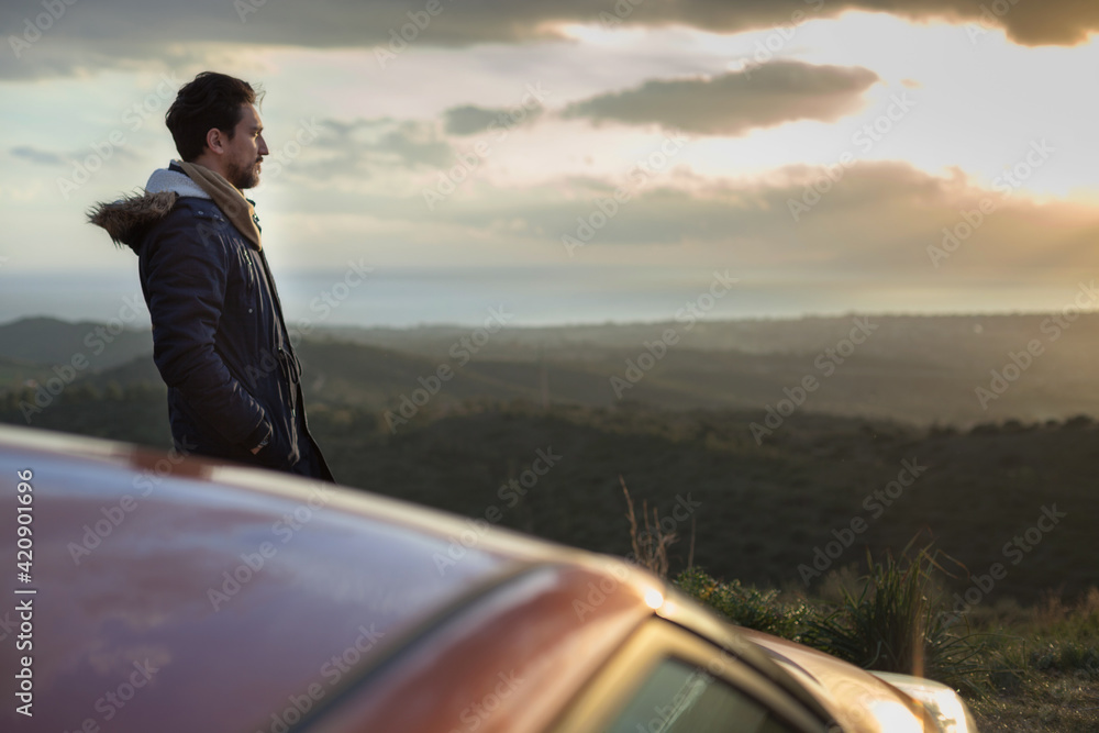 Man resting against car on roadside, enjoying view on hilltop Man resting against car on roadside, enjoying view on hilltop