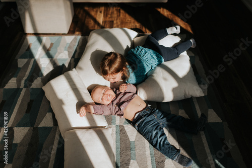 Baby boy and toddler sister lying on cushions on living room floor, overhead view photo