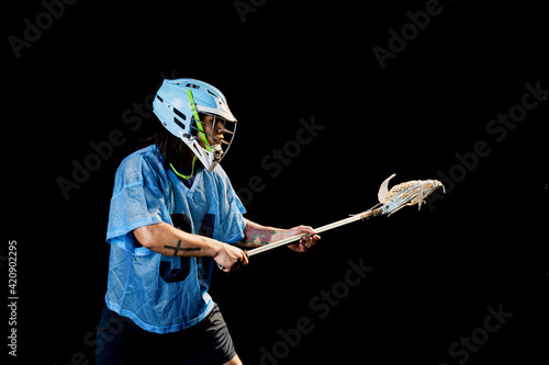 Young male lacrosse player poised with lacrosse stick, against black background photo