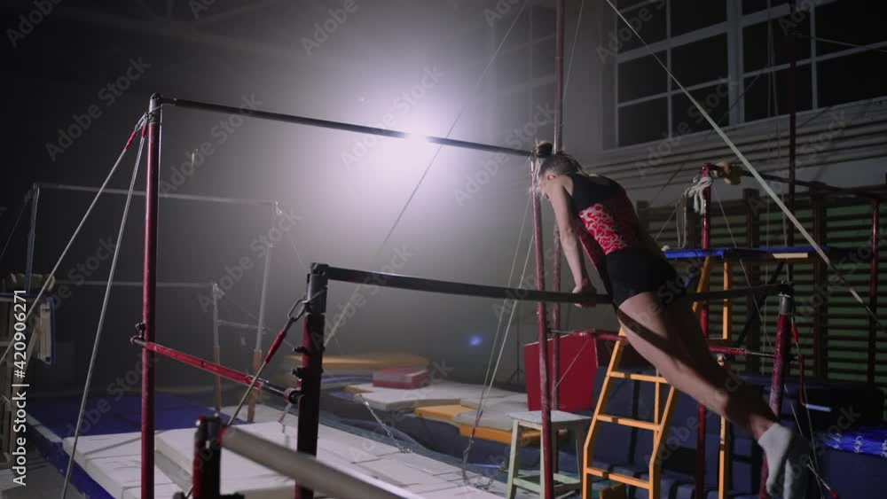 sporty female gymnast is performing exercises on uneven bars in ...