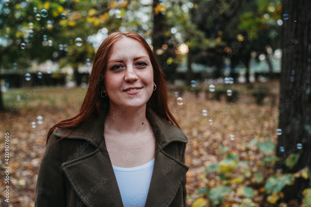 Young woman with long red hair amongst floating bubbles in autumn park, head and shoulder portrait Young woman with long red hair amongst floating bubbles in autumn park, head and shoulder portrait