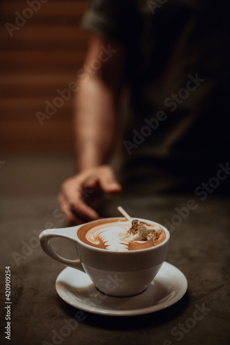 Barista at cafe counter with cup of mocha topped with toasted marshmallow, cropped shallow focus