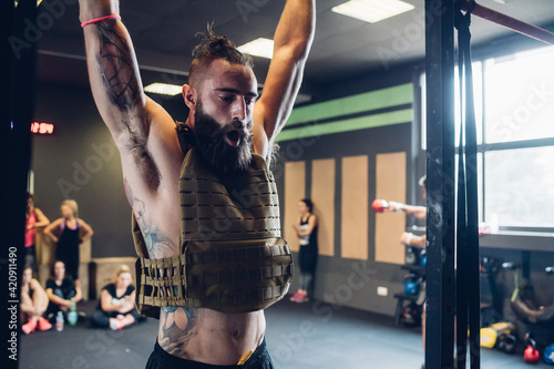 Young tattooed man training in gym, hanging from exercise bar