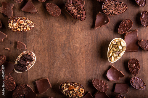 Canvas Print Top view of lots of mini stuffed chocolate easter eggs and cracked chocolates on a wooden table with free space in the middle