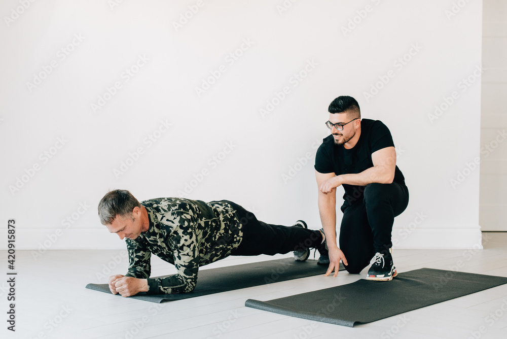 Fitness instructor observing man doing plank in studio Fitness instructor observing man doing plank in studio