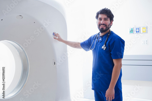 Young male radiographer operating CT scanner in radiology department, portrait photo