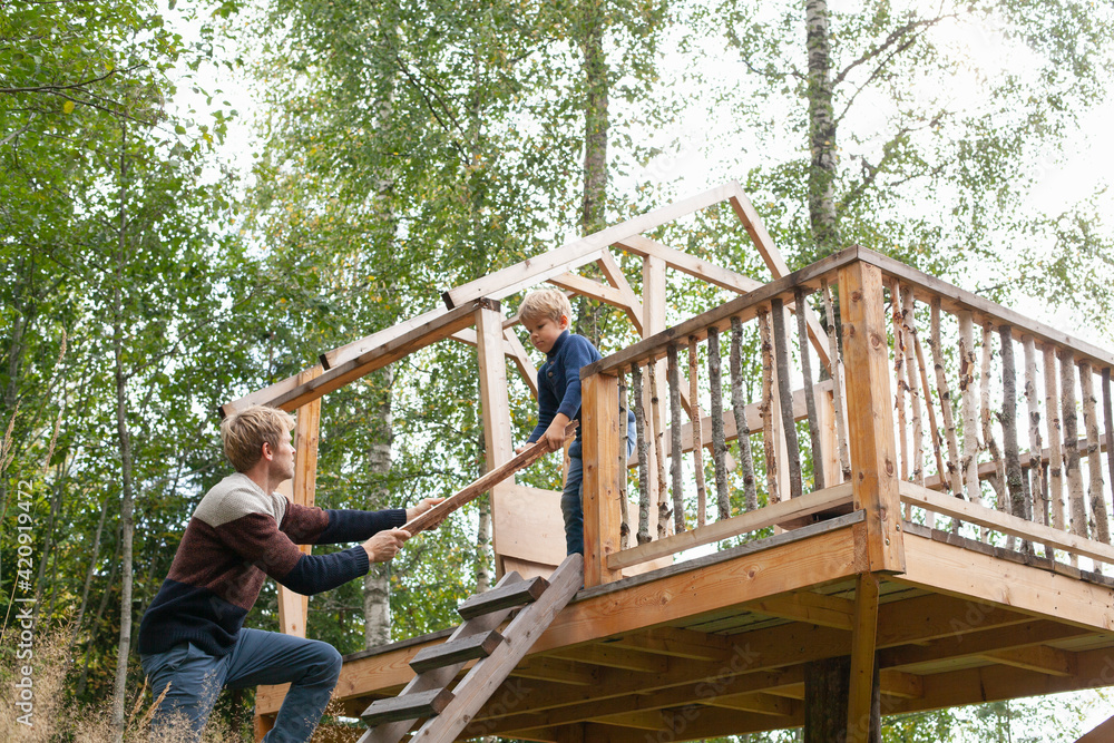 Father and son building treehouse together in garden Father and son building treehouse together in garden