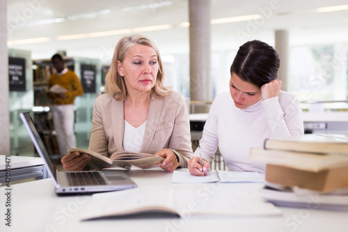 Female teacher working with girl student in university library. High quality photo