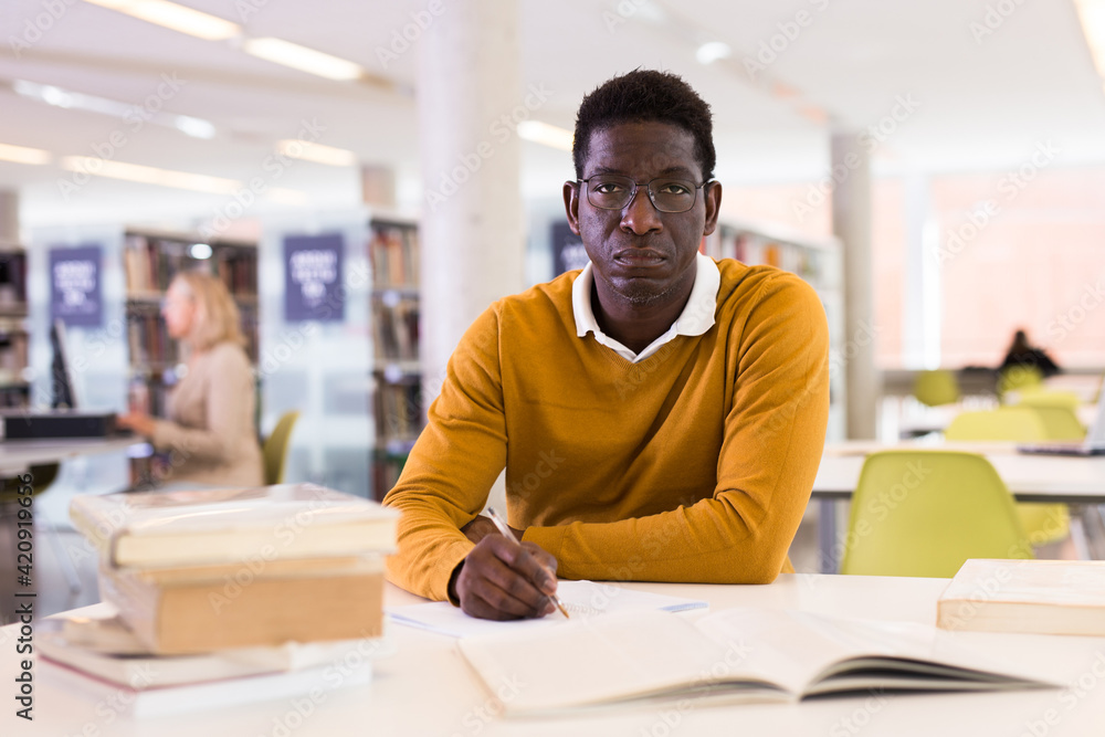 Fototapeta premium Portrait of confident african-american male student working with book in public library. High quality photo