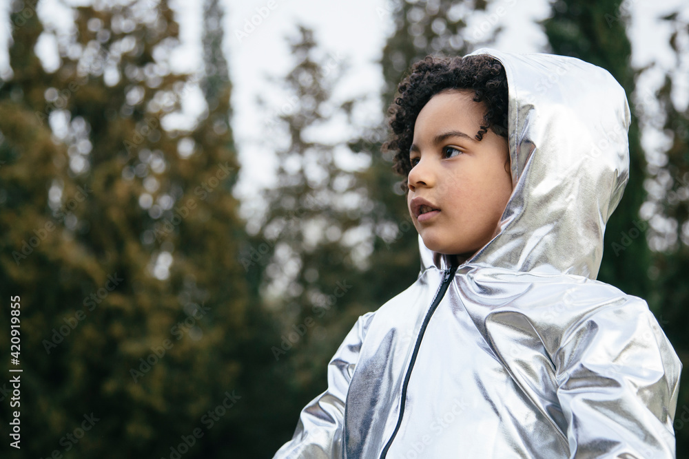 Black boy wearing a silver clothing, looking away. In a park background. Copyspace. Kids, astronauts, extraterrestrials and black people concept Black boy wearing a silver clothing, looking away. In a park background. Copyspace. Kids, astronauts, extraterrestrials and black people concept