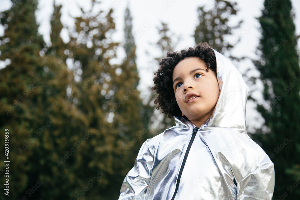Black boy wearing a silver clothing, looking up. In a park background. Copyspace. Kids, astronauts, extraterrestrials and black people concept Black boy wearing a silver clothing, looking up. In a park background. Copyspace. Kids, astronauts, extraterrestrials and black people concept