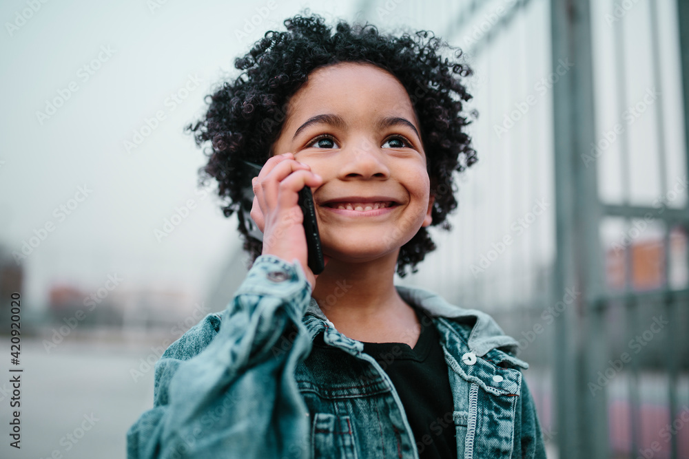 Afro child talking on his mobile phone, smiling, with an enthusiasm and happiness expression. In a courts background. Kids, smartphones and black people concept. Afro child talking on his mobile phone, smiling, with an enthusiasm and happiness expression. In a courts background. Kids, smartphones and black people concept.
