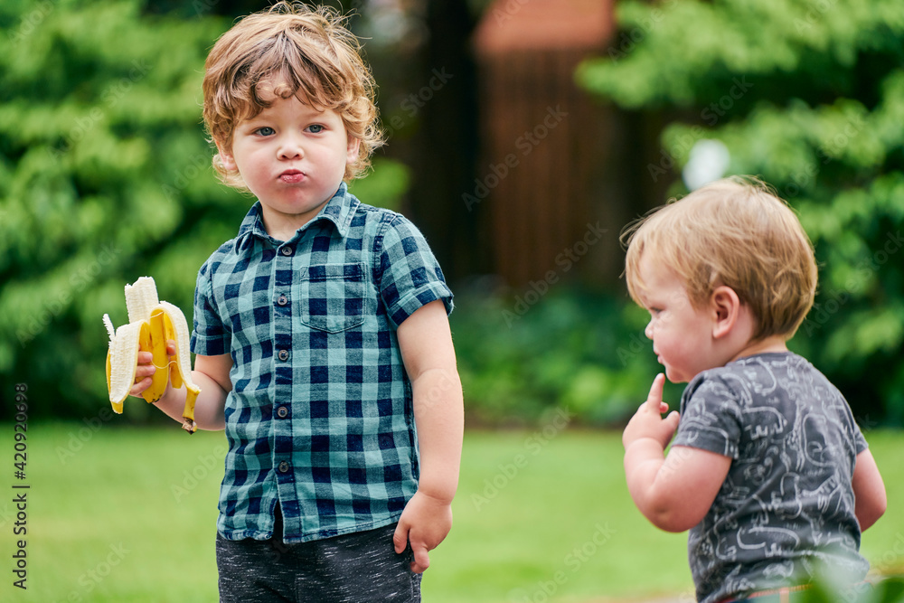 Toddlers exploring and eating banana in park Toddlers exploring and eating banana in park