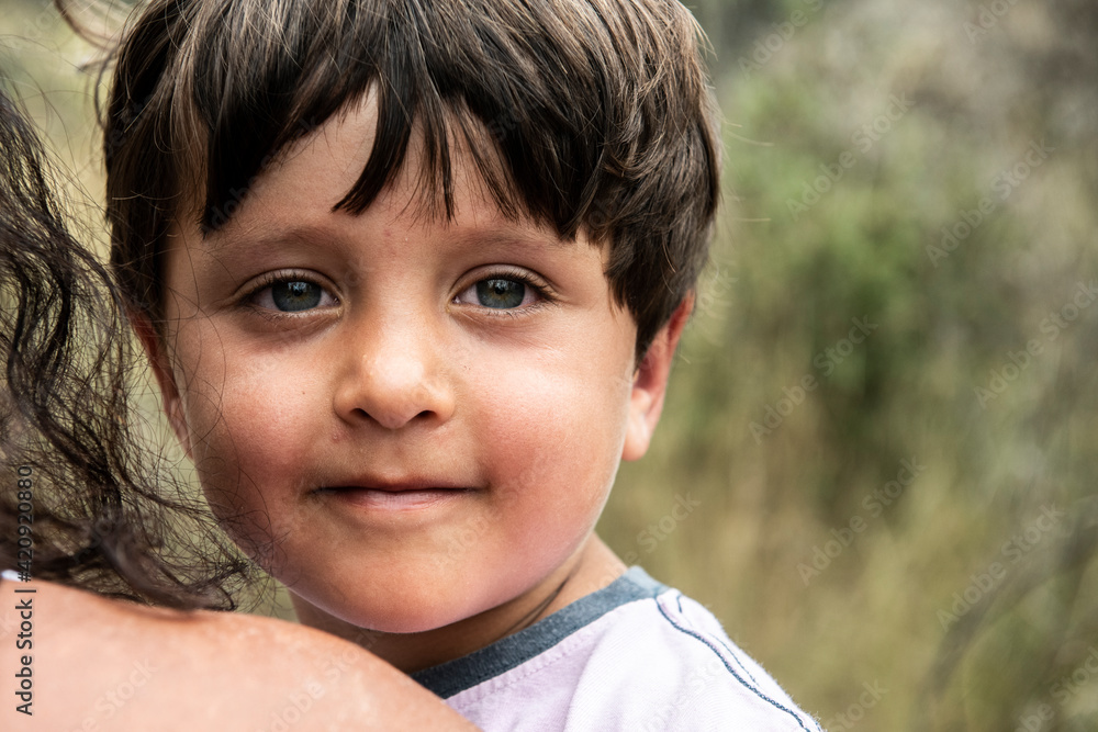Portrait of young boy with brown hair being carried by his mother, looking at camera. Portrait of young boy with brown hair being carried by his mother, looking at camera.