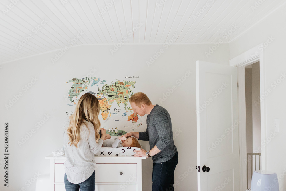 Couple changing toddler's diaper on changing table Couple changing toddler's diaper on changing table