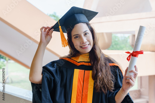 The Asian university graduates in graduation gown and a mortarboard cap with a degree certificate in hand celebrating education achievement in the commencement ceremony. Congratulations to graduations