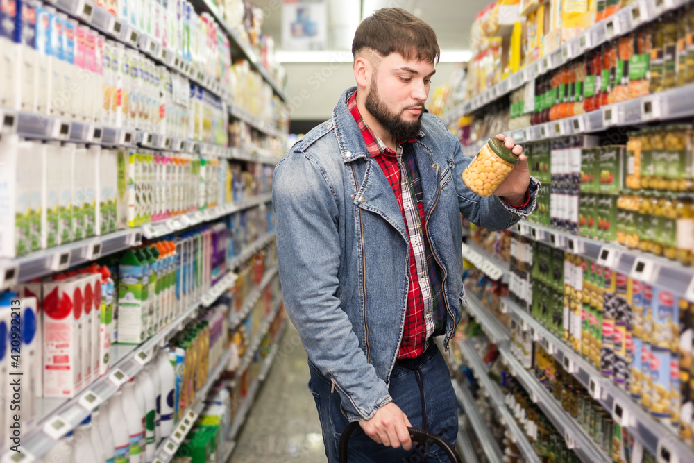 Focused bearded guy choosing organic pickles during shopping at grocery store