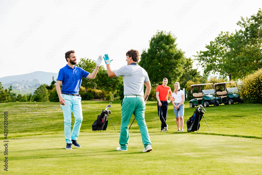 Friends giving high five on golf course, couple watching in background Friends giving high five on golf course, couple watching in background