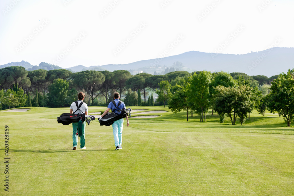 Friends carrying golf bag walking on golf course Friends carrying golf bag walking on golf course
