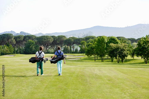 Friends carrying golf bag walking on golf course photo