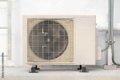 Condenser unit or compressor outside home or residential building. Unit of central air conditioner (AC) or heating ventilation air conditioning system (HVAC). Electric fan and refrigerant pump inside.