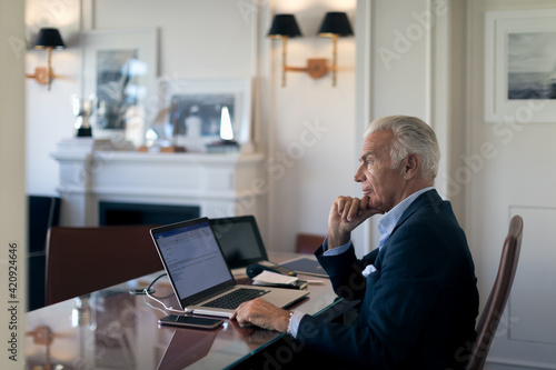 Senior businessman sitting at desk, looking at laptop.