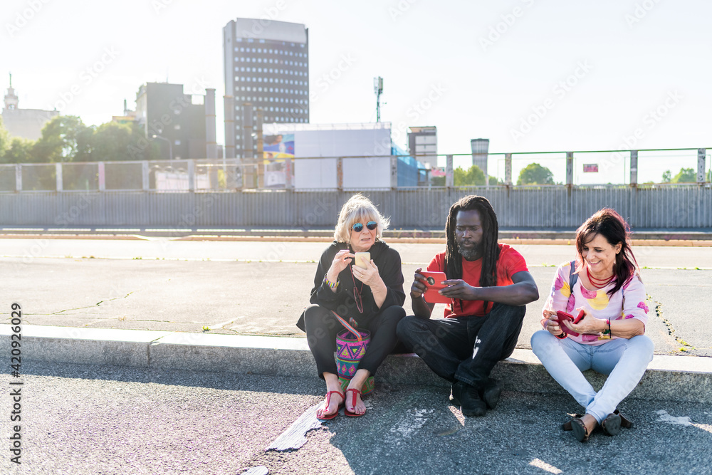 Black man with dreadlocks and two Caucasian women sitting on sidewalk, checking their mobile phones. Black man with dreadlocks and two Caucasian women sitting on sidewalk, checking their mobile phones.