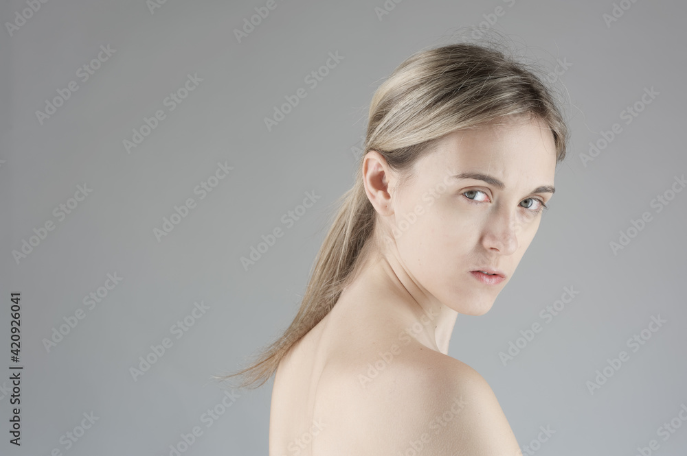 Head and shoulders portrait of nude young woman with blond hair in ponytail, looking at camera, on grey background. Head and shoulders portrait of nude young woman with blond hair in ponytail, looking at camera, on grey background.