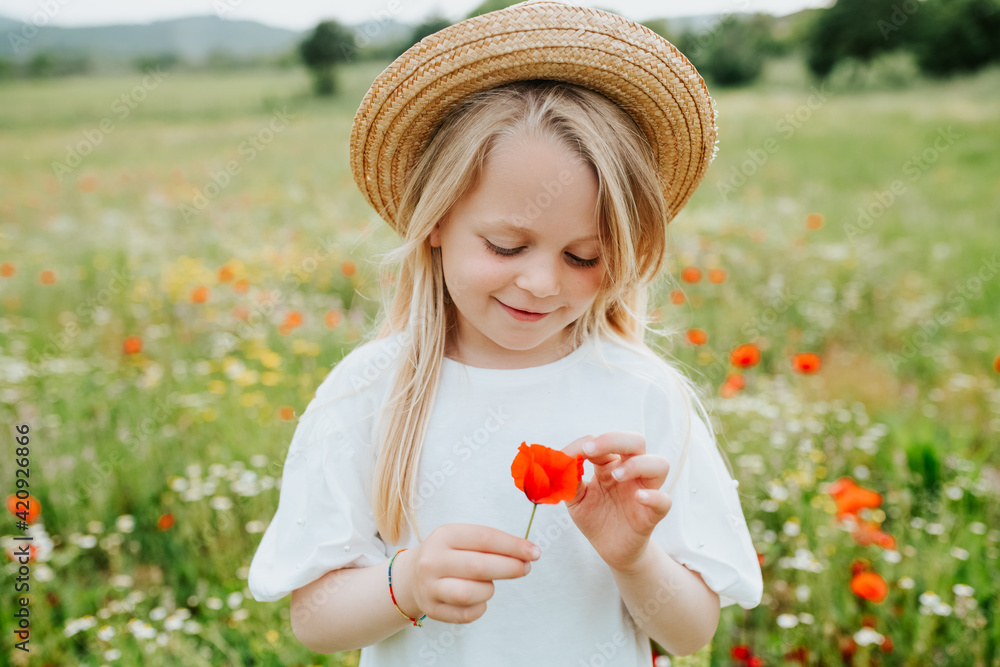 Portrait of young girl holding a poppy, standing in a meadow of wild flowers. Portrait of young girl holding a poppy, standing in a meadow of wild flowers.