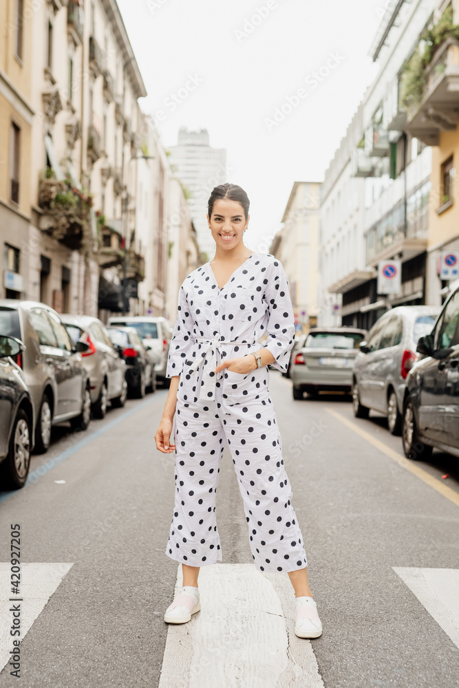 Portrait of smiling woman wearing white and black polka dot jumpsuit, standing on pedestrian crossing. Portrait of smiling woman wearing white and black polka dot jumpsuit, standing on pedestrian crossing.