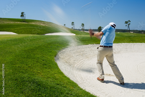 Male golfer chipping out of sand trap. 