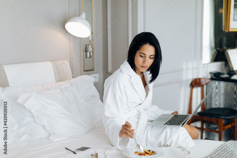Woman using laptop and having breakfast in suite Woman using laptop and having breakfast in suite
