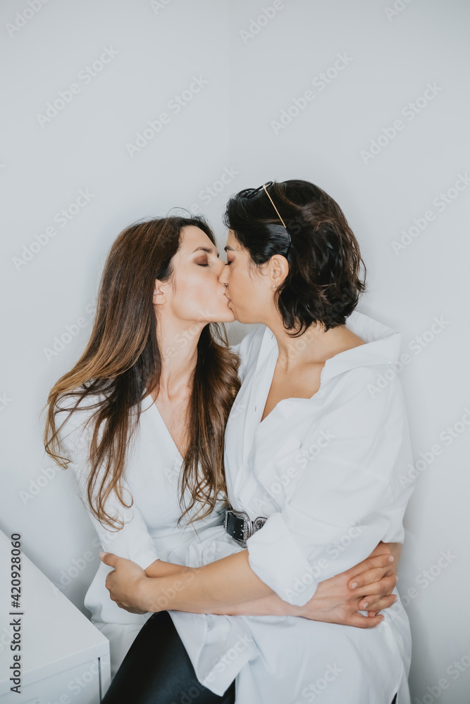 Portrait of two women with brown hair embracing and kissing.