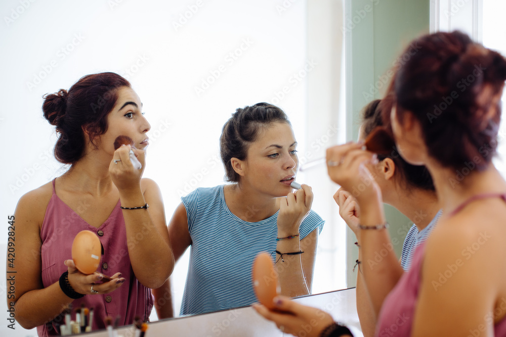 Friends putting on makeup at mirror Friends putting on makeup at mirror