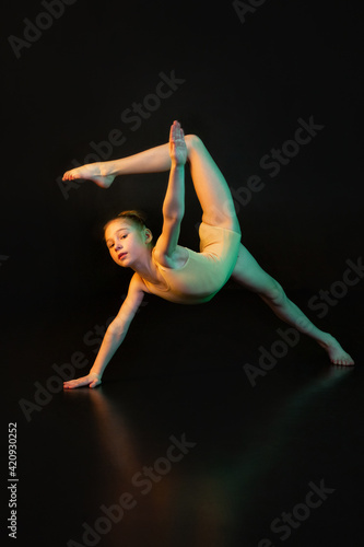 Balance. A girl is a young athlete, a gymnast in a pose in isolation on a black studio background in neon mixed color light.