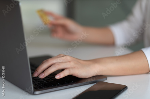 Close up hand of woman using laptop computer and credit card for shopping online at home.