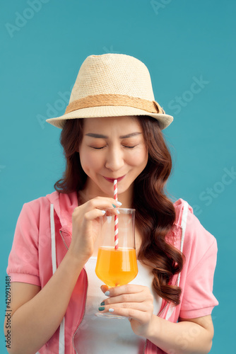 Attractive young Asian woman drinking fruit juice over blue background.